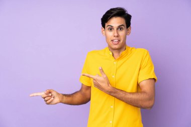 İzole edilmiş mor arka plandaki adam şaşırmış ve işaret ediyor.