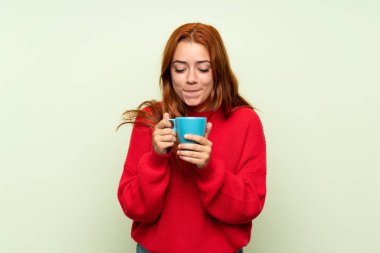 Izole yeşil arka plan üzerinde kazak ile genç redhead kız kahve sıcak fincan tutarak
