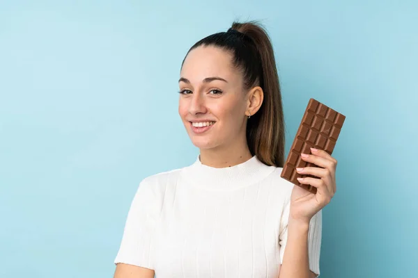 Young Brunette Woman Isolated Blue Background Taking Chocolate Tablet Happy — 스톡 사진