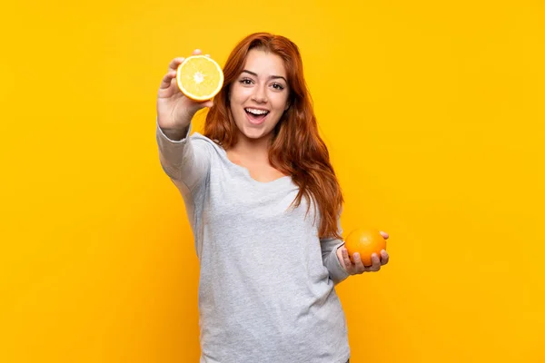 Adolescente rousse fille tenant une orange sur fond jaune isolé — Photo