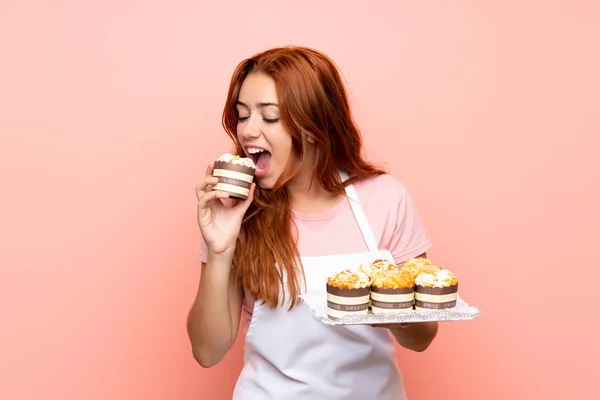 Tiener Redhead meisje houdt veel van verschillende mini cakes over geïsoleerde roze achtergrond — Stockfoto