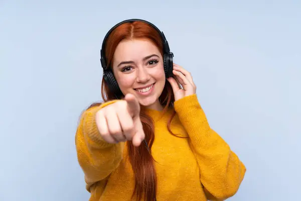 Redhead Teenager Dívka Přes Izolované Modré Pozadí Poslech Hudby Ukazuje — Stock fotografie