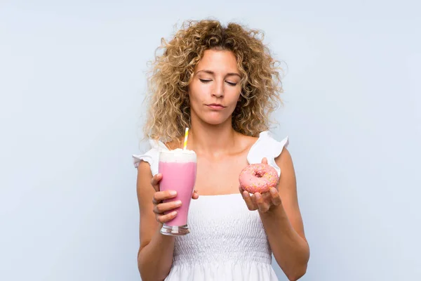 Jeune femme blonde aux cheveux bouclés tenant un milkshake aux fraises et un beignet — Photo