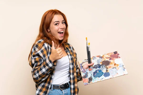 Adolescente Rossa Ragazza Tenendo Una Tavolozza Sfondo Isolato Dando Pollice — Foto Stock