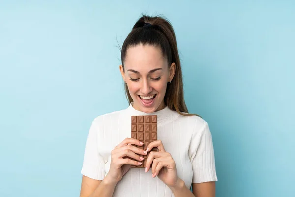 Jovem Morena Sobre Fundo Azul Isolado Comendo Comprimido Chocolate — Fotografia de Stock