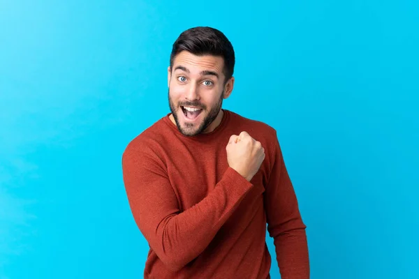 Sakallı Yakışıklı Genç Adam Mavi Arka Planda Zaferi Kutluyor — Stok fotoğraf