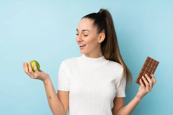 Young Brunette Woman Isolated Blue Background Taking Chocolate Tablet One — 스톡 사진