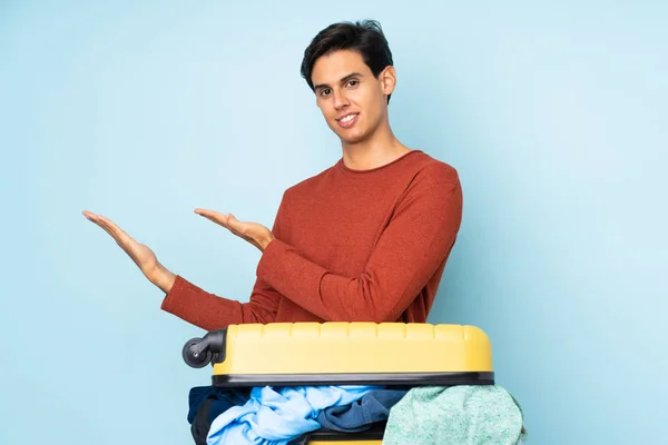 Hombre Con Una Maleta Llena Ropa Sobre Fondo Azul Aislado —  Fotos de Stock