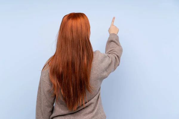 Redhead Teenager Dívka Svetrem Přes Izolované Modré Pozadí Ukazuje Zpět — Stock fotografie