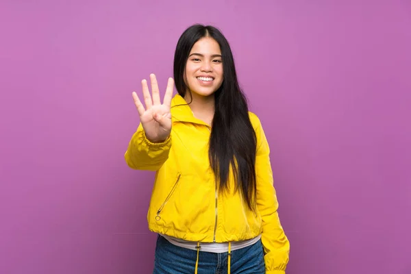 年轻的少年亚洲女孩在孤立的紫色背景上快乐地数着四个手指 — 图库照片