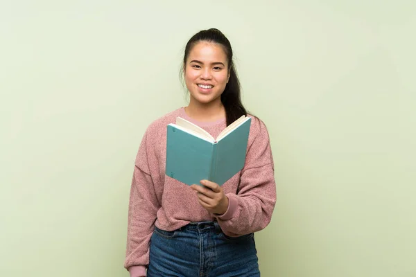 孤立した緑の背景の上に若いティーンエイジャーアジアの女の子が本を保持し 読んで — ストック写真