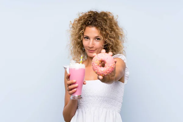 Молодая блондинка с вьющимися волосами с клубничным молочным коктейлем и пончиком — стоковое фото