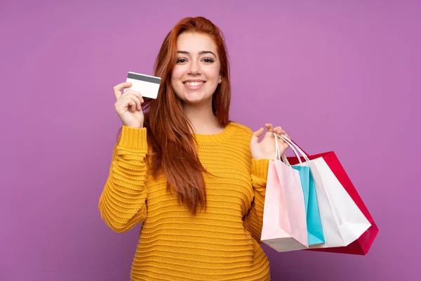 Roodharige Tiener Meisje Geïsoleerde Paarse Achtergrond Holding Boodschappentassen Een Creditcard — Stockfoto