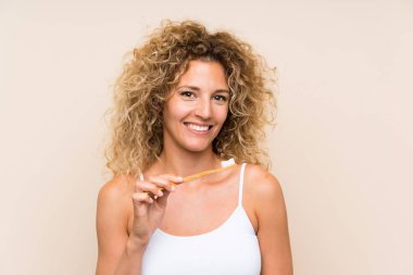 Kıvırcık saçlı genç sarışın kadın dişlerini fırçalıyor