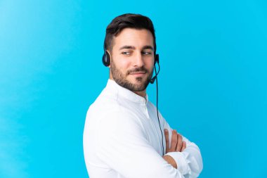 Tele pazarlamacı, mavi arka planda kulaklıkla gülerek çalışıyor.