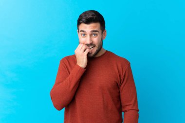 Sakallı, genç ve yakışıklı bir adam mavi arka planda gergin ve korkmuş.