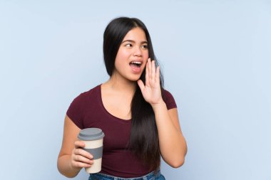 Young teenager Asian girl holding a take away coffee shouting with mouth wide open