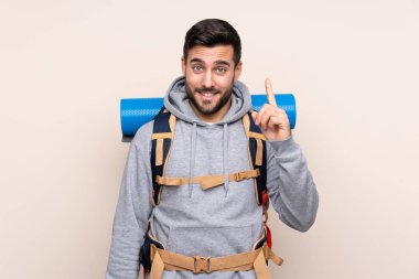 Arka planda izole edilmiş büyük bir sırt çantası olan genç dağcı, işaret parmağıyla işaret etmek harika bir fikir.