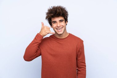 İzole edilmiş mavi arka planda genç beyaz bir adam telefon jesti yapıyor. Bana geri dönüş işareti ver.