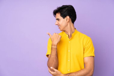 İzole edilmiş mor arka planda bir adam bir ürünü sunmak için kenarı işaret ediyor.