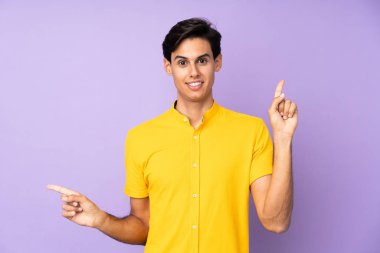 İzole edilmiş mor arka plandaki adam parmak uçlarını işaret ediyor ve mutlu.