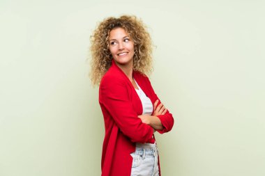 Sarışın, kıvırcık saçlı, yalıtılmış yeşil bir geçmişi olan, kolları çapraz ve mutlu genç bir kadın.