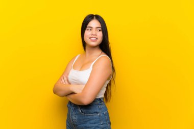 Young teenager Asian girl over isolated yellow background with arms crossed and happy