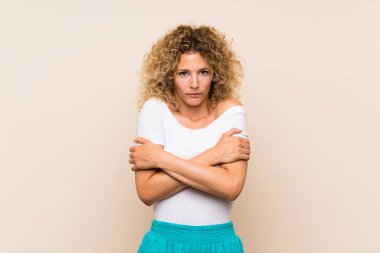 Kıvırcık saçlı, soyutlanmış arka planda donan genç sarışın kadın.