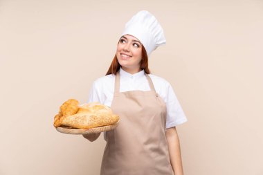 Şef üniformalı kızıl saçlı genç kız. Kadın fırıncı elinde birkaç ekmek olan bir masa tutarken gülümsüyor.