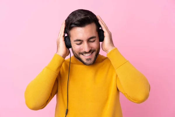 Jovem homem bonito com barba ouvindo música sobre rosa isolado — Fotografia de Stock