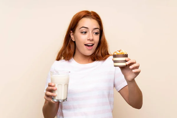 Tinédzser vöröshajú lány kezében egy pohár tejet és egy muffin alatt elszigetelt háttér — Stock Fotó