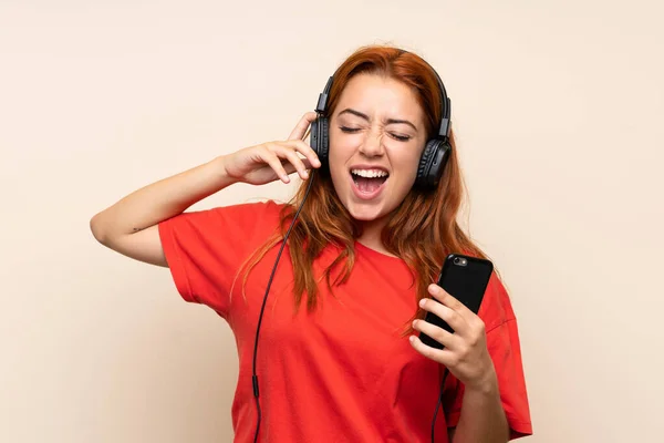 Подросток рыжая девушка слушает музыку с мобильного на изолированном фоне — стоковое фото
