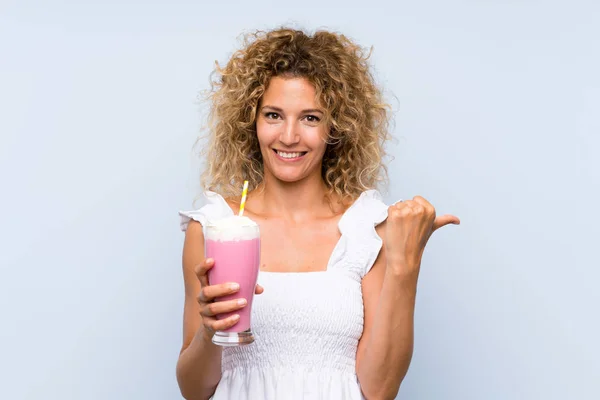 Young Blonde Woman Curly Hair Holding Strawberry Milkshake Pointing Side — 스톡 사진
