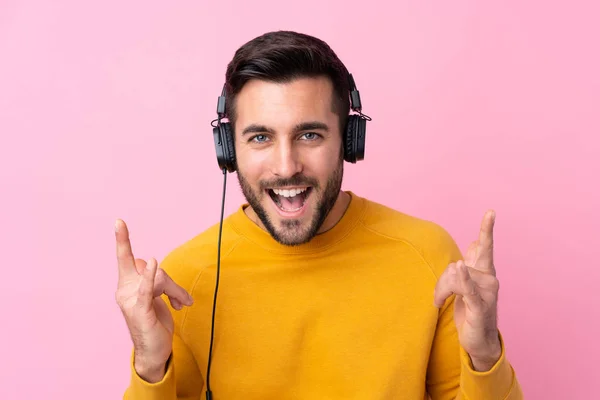 Jovem homem bonito com barba ouvindo música sobre rosa isolado — Fotografia de Stock