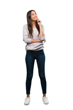A full-length shot of a Young hispanic brunette woman thinking an idea while looking up over isolated white background