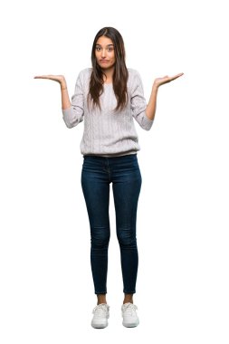 A full-length shot of a Young hispanic brunette woman having doubts while raising hands over isolated white background
