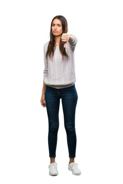 A full-length shot of a Young hispanic brunette woman showing thumb down with negative expression over isolated white background