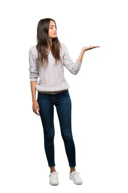 A full-length shot of a Young hispanic brunette woman holding copyspace with doubts over isolated white background
