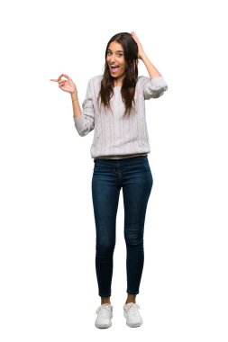 A full-length shot of a Young hispanic brunette woman surprised and pointing finger to the side over isolated white background