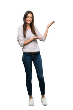 A full-length shot of a Young hispanic brunette woman extending hands to the side for inviting to come over isolated white background