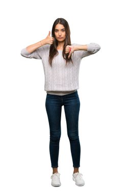 A full-length shot of a Young hispanic brunette woman making good-bad sign. Undecided between yes or not over isolated white background