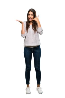 A full-length shot of a Young hispanic brunette woman making phone gesture and doubting over isolated white background