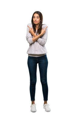 A full-length shot of a Young hispanic brunette woman pointing to the laterals having doubts over isolated white background