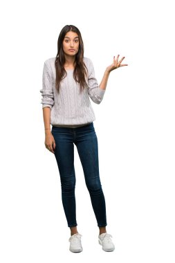 A full-length shot of a Young hispanic brunette woman making doubts gesture over isolated white background