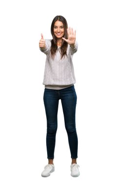 A full-length shot of a Young hispanic brunette woman counting six with fingers over isolated white background