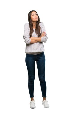 A full-length shot of a Young hispanic brunette woman making doubts gesture while lifting the shoulders over isolated white background