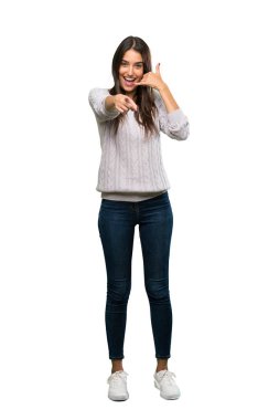 A full-length shot of a Young hispanic brunette woman making phone gesture and pointing front over isolated white background
