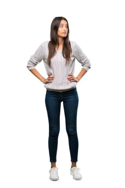 A full-length shot of a Young hispanic brunette woman making doubts gesture looking side over isolated white background