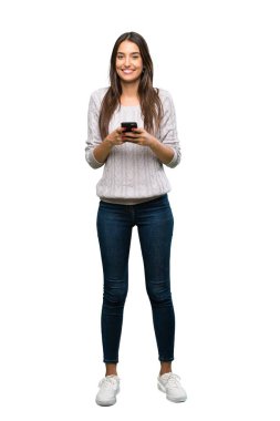A full-length shot of a Young hispanic brunette woman sending a message with the mobile over isolated white background