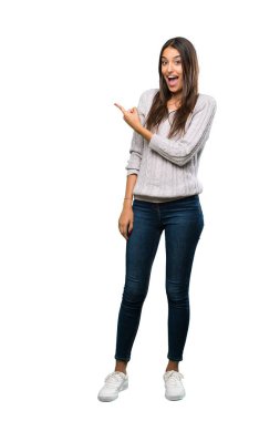 A full-length shot of a Young hispanic brunette woman surprised and pointing side over isolated white background